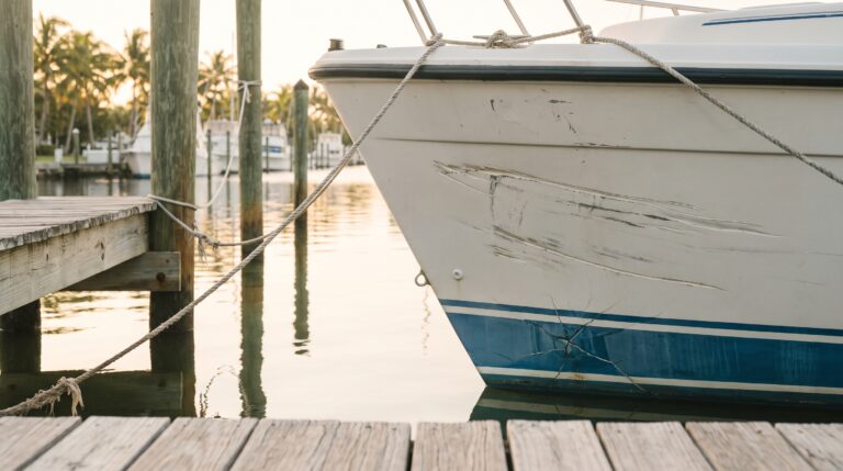 Close-up of a fiberglass boat hull with deep gelcoat scratches and a cracked section near the waterline